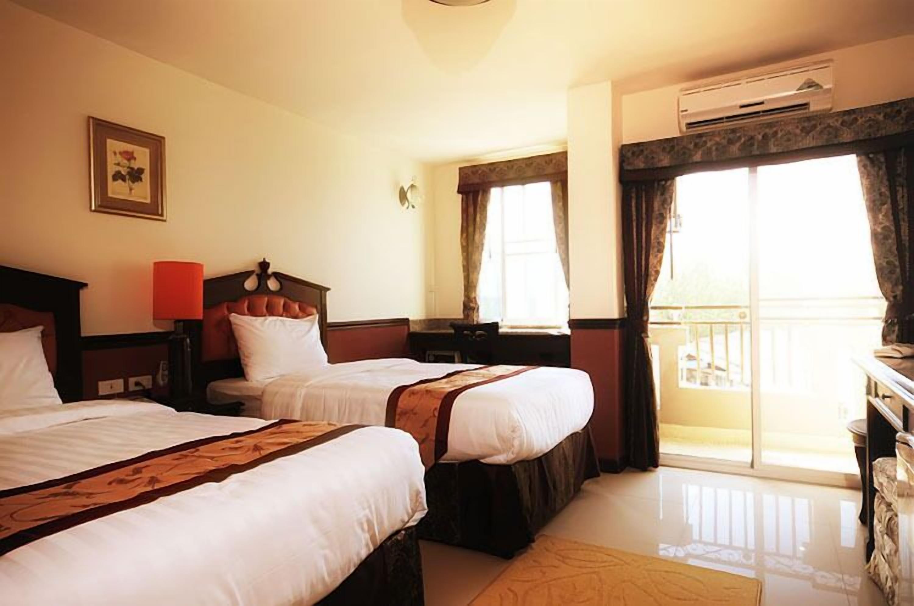 Habitación de hotel con dos camas, una mesita de noche, una lámpara, una ventana con cortinas y un equipo de aire acondicionado.