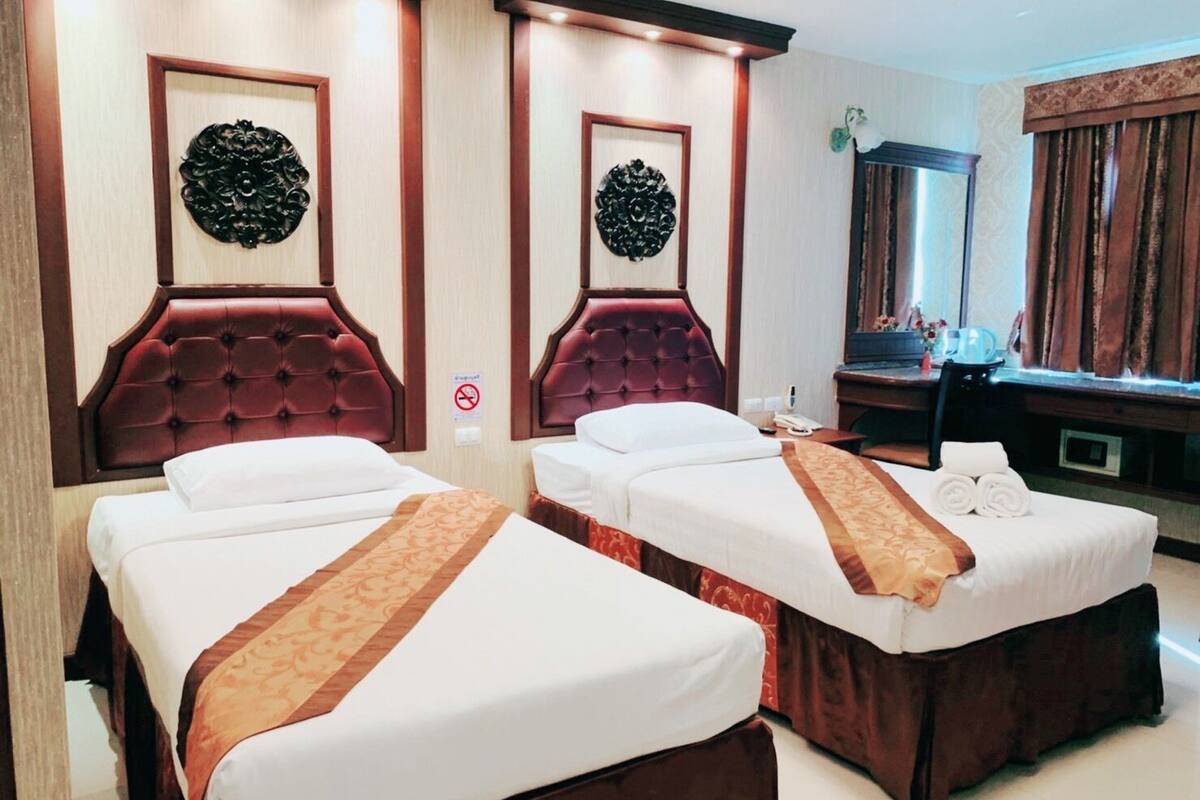 Een hotelkamer met twee bedden, elk met een rode hoofdbord en een decoratief kunstwerk erboven.
