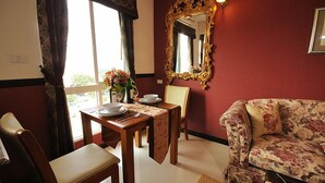 A dining area with a table set for two, a floral sofa, and a large ornate mirror on the wall. - The Airport Greenery Hotel (Chiang Mai)