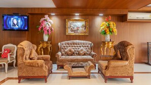 A lobby with a tufted sofa, two armchairs, a coffee table, a TV, and two flower arrangements. - The Airport Greenery Hotel (Chiang Mai)