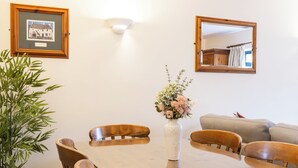 A dining area with a glass-top table, wooden chairs, a vase with flowers, a framed picture on the wall, and a mirror. - The Uplands Serviced Apartments (St. Helier)