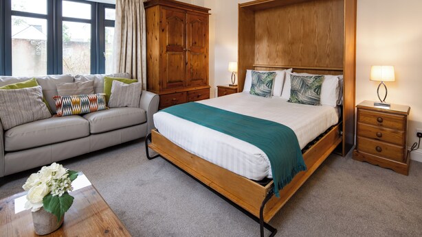 A bedroom with a bed, wooden wardrobe, bedside table, and a sofa. - The Uplands Serviced Apartments (St. Helier)