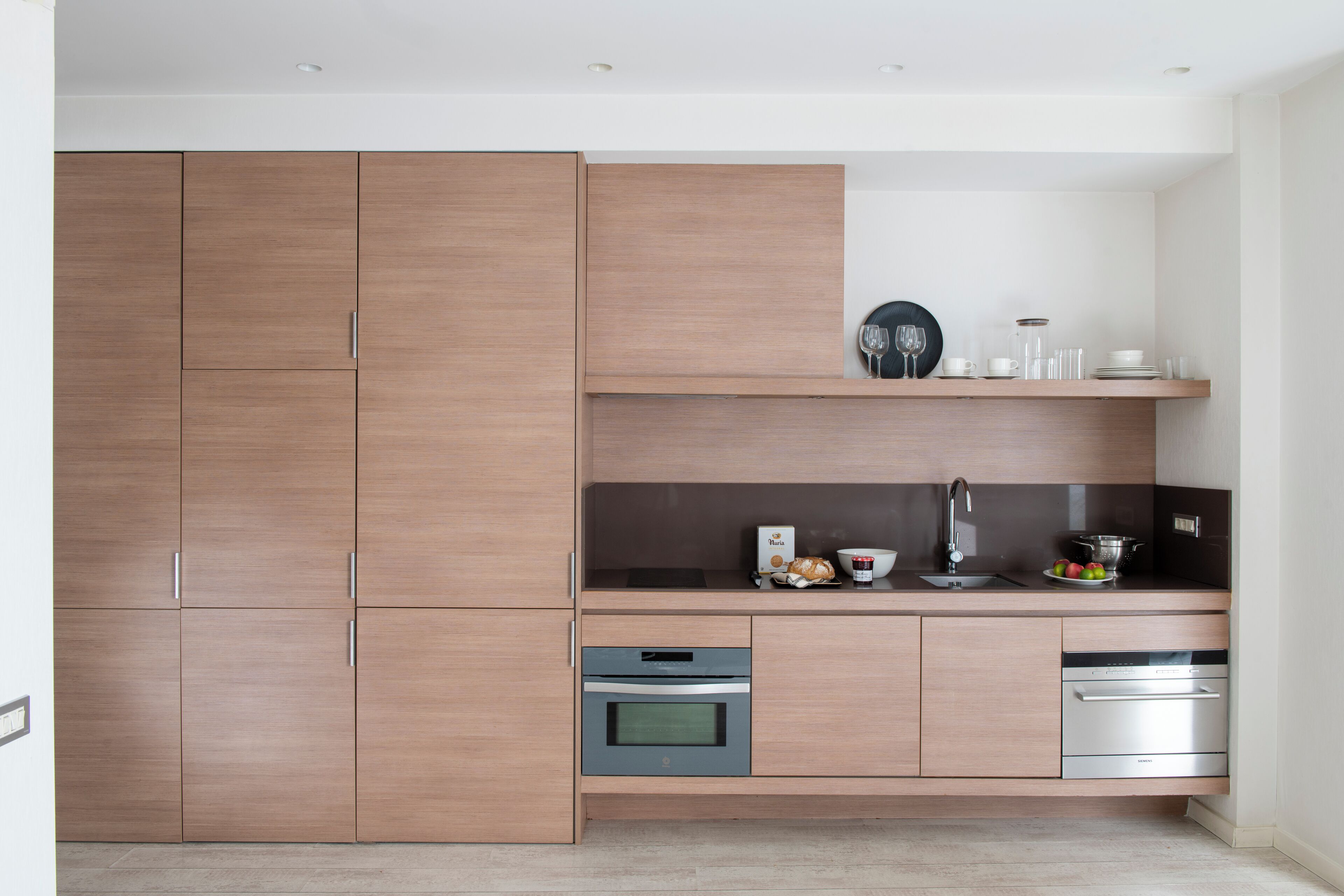 Een moderne keuken met houten kastjes, een inbouwoven, een vaatwasser en een aanrecht met een spoelbak en diverse keukengerei.