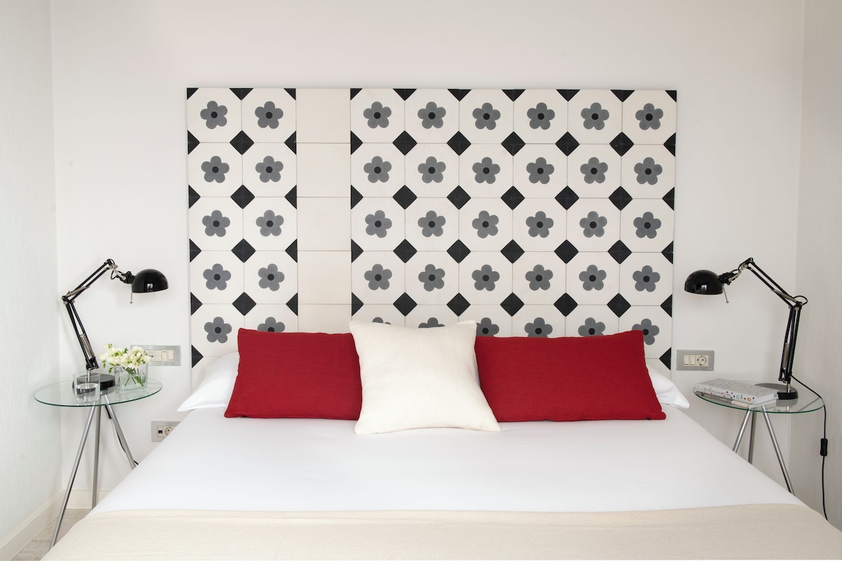 A hotel room with a bed, two bedside tables, and a wall with a geometric pattern.