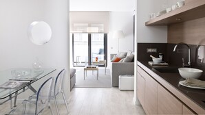 Una cocina moderna con una mesa de comedor de vidrio, sillas traslúcidas, un sofá gris y una encimera negra con un fregadero y un lavabo.