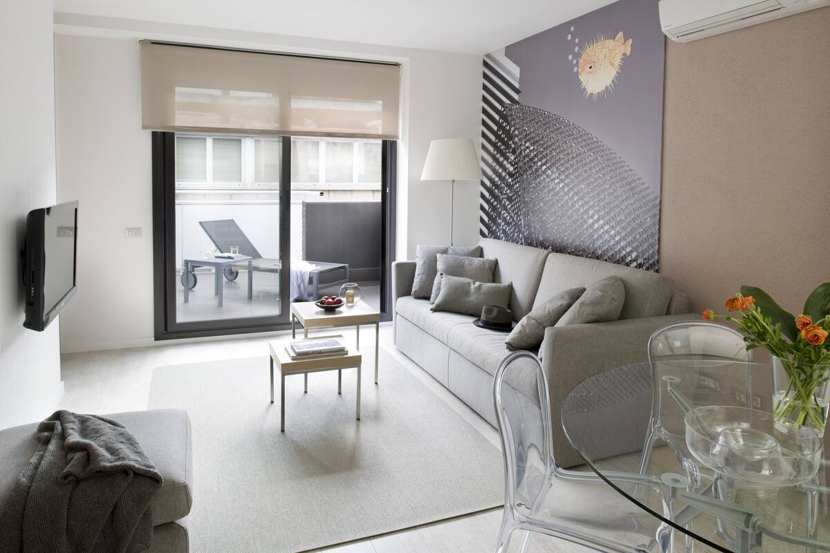 Una sala de estar moderna con un sofá, una mesa de centro de vidrio, una silla transparente y un televisor montado en la pared.