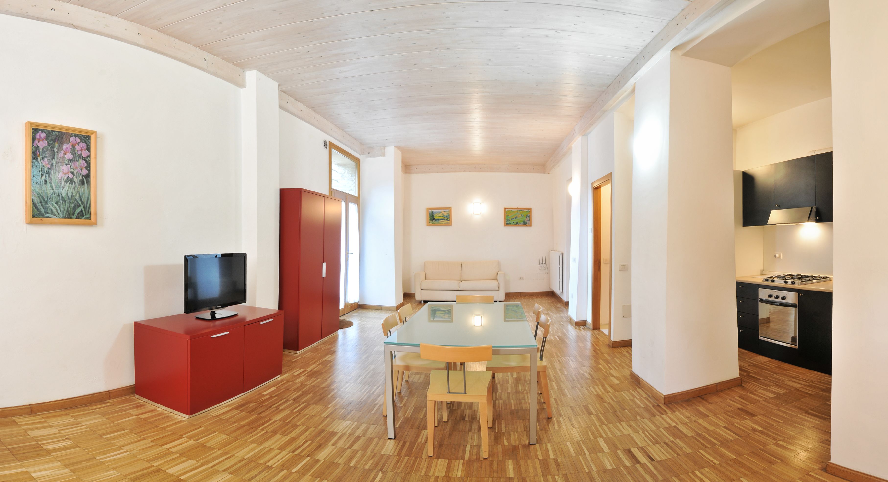 Uma sala de estar moderna com uma mesa de jantar de vidro, um móvel de entretenimento vermelho e uma área de cozinha com fogão.