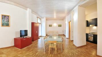 Uma sala de estar moderna com uma mesa de jantar de vidro, um móvel de entretenimento vermelho e uma área de cozinha com fogão.