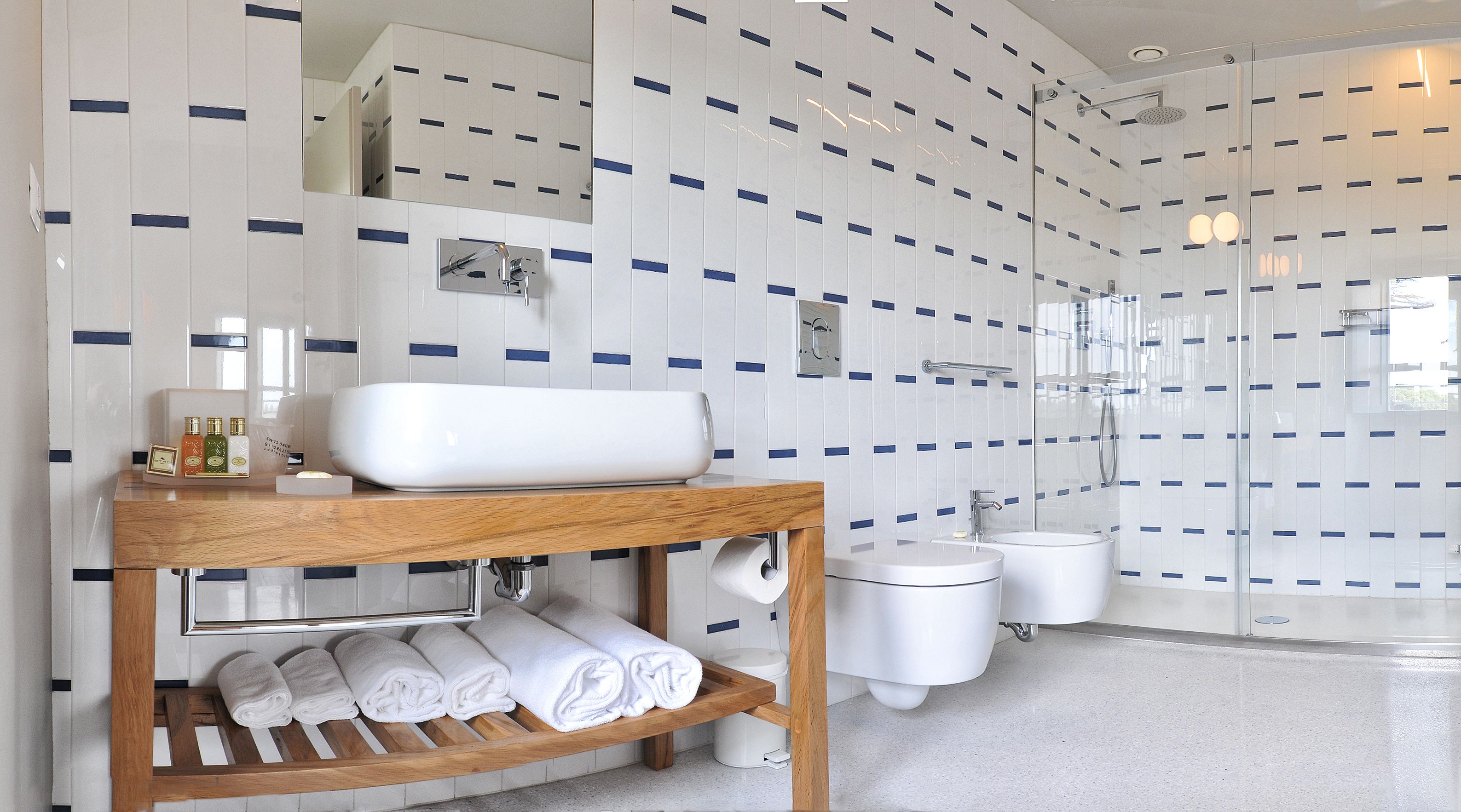 A modern bathroom with a wooden vanity, a large mirror, a toilet, a bidet, and a glass-enclosed shower area.