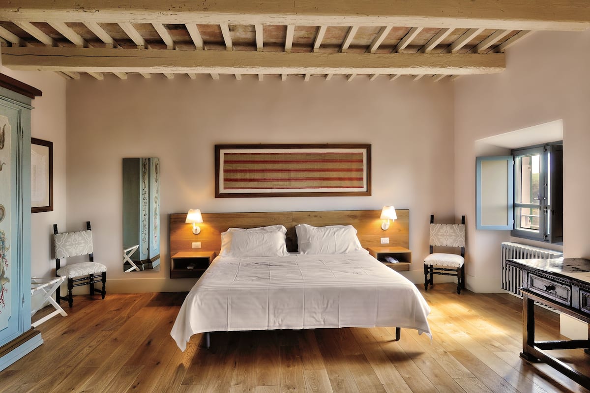 A bedroom with a large bed, two bedside tables with lamps, a wooden ceiling, and a window with a view.