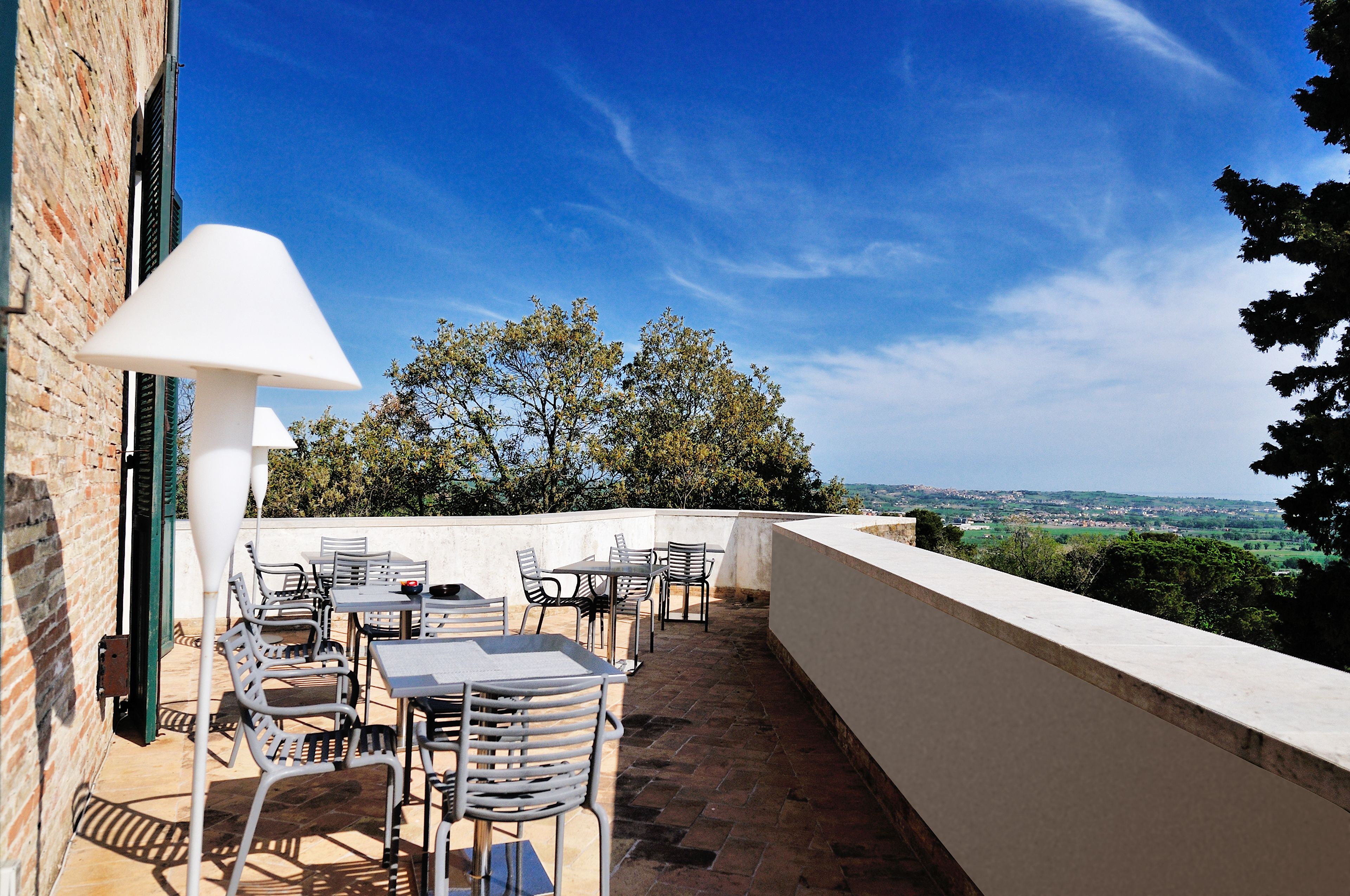 Un patio al aire libre con mesas y sillas, una lámpara blanca, y vistas a árboles y un paisaje distante.