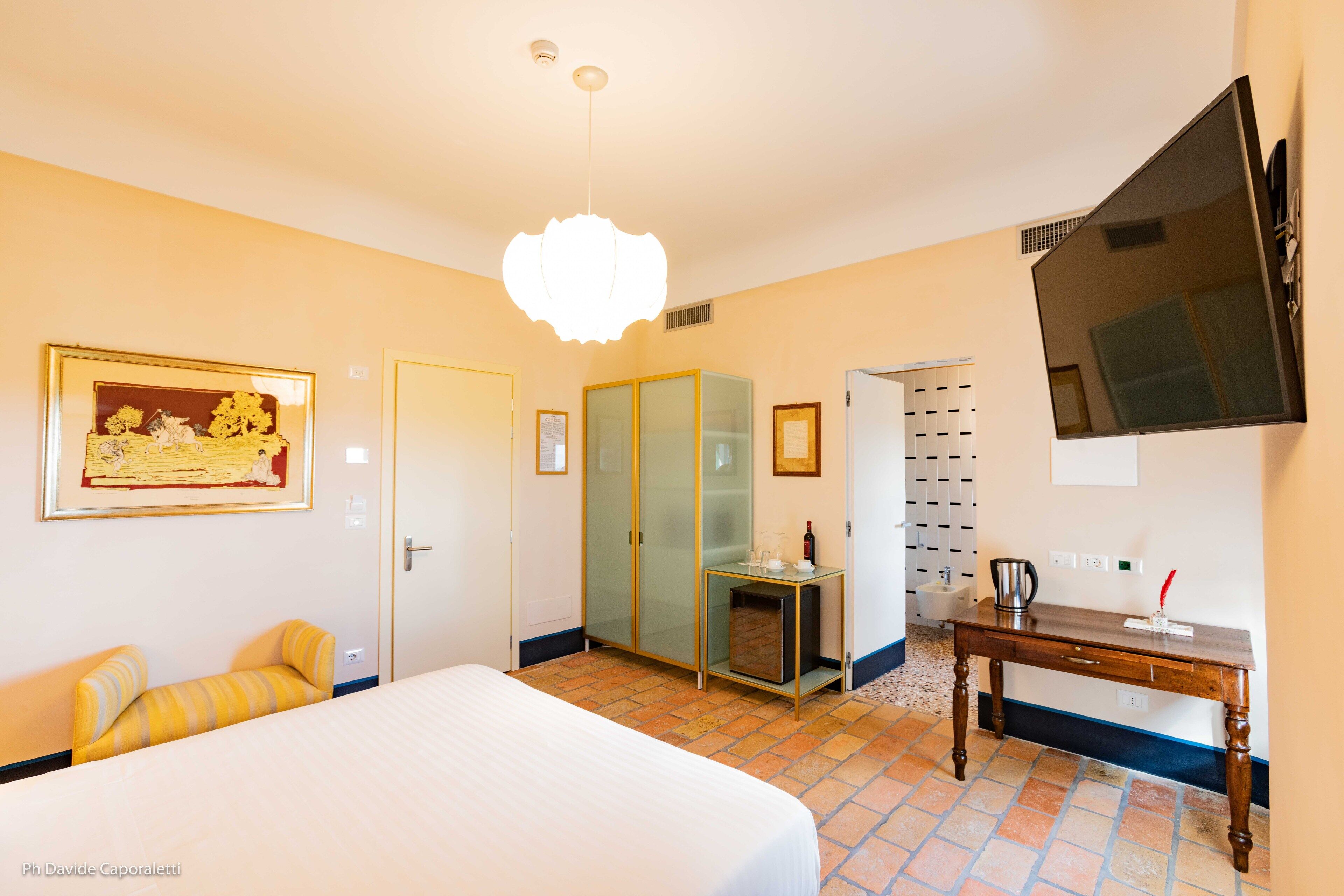 A hotel room with a bed, a desk, a television, a painting, and a door.