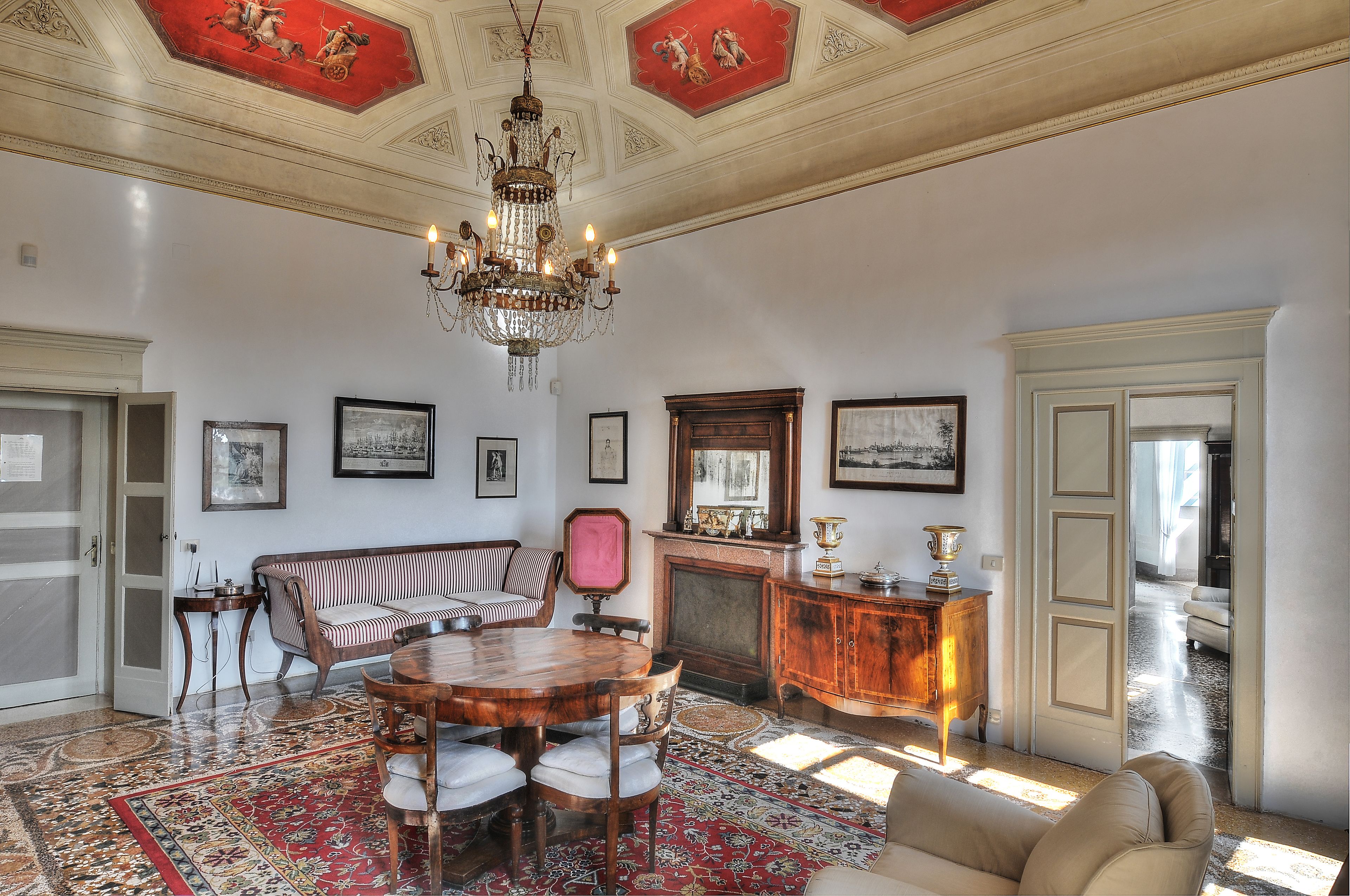 Ein geräumiges Zimmer mit einem großen Chandelier, einem runden Holzesstisch, einer Couch und einem Kamin.