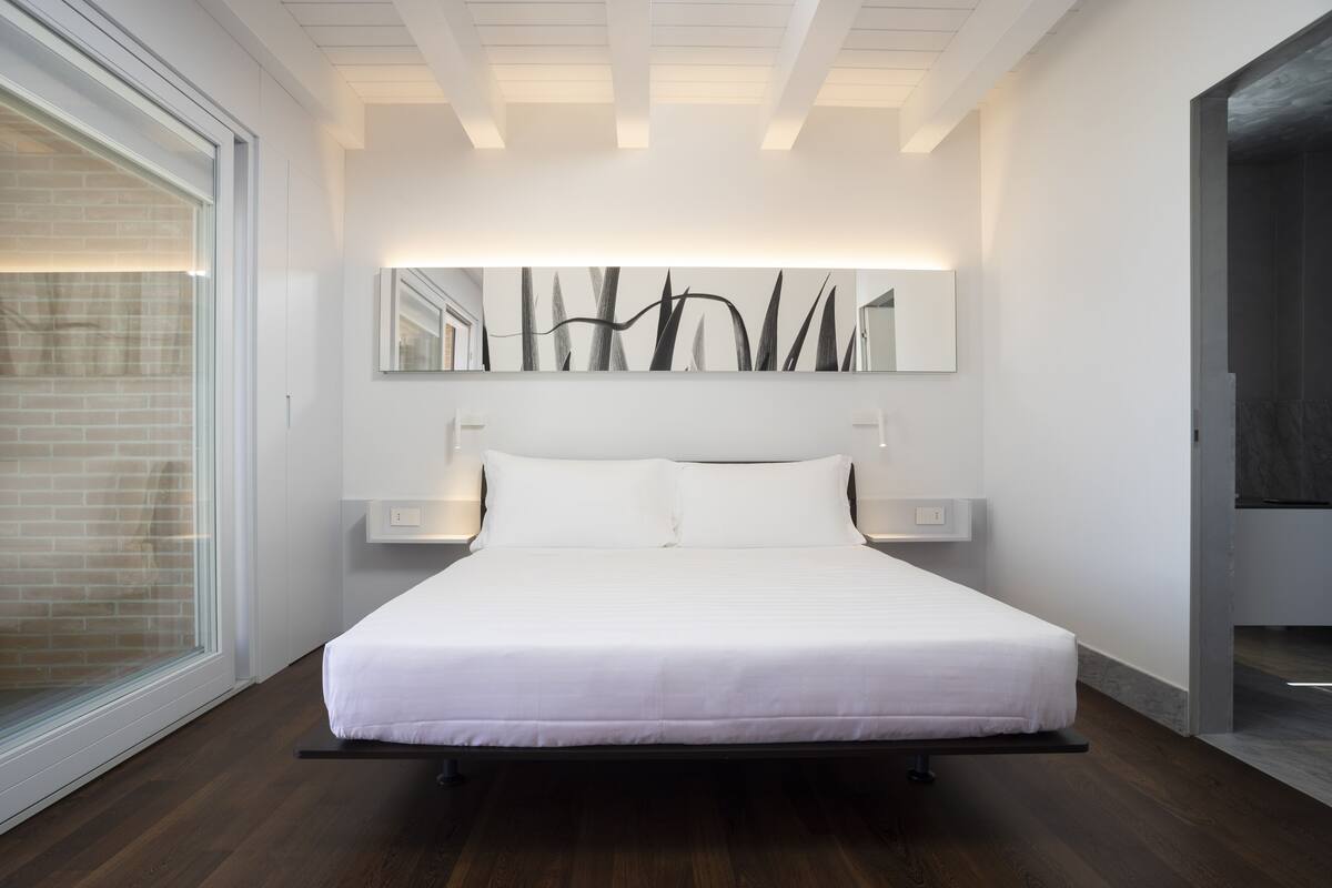 A modern bedroom with a large bed, a wall-mounted mirror, and bedside lamps.