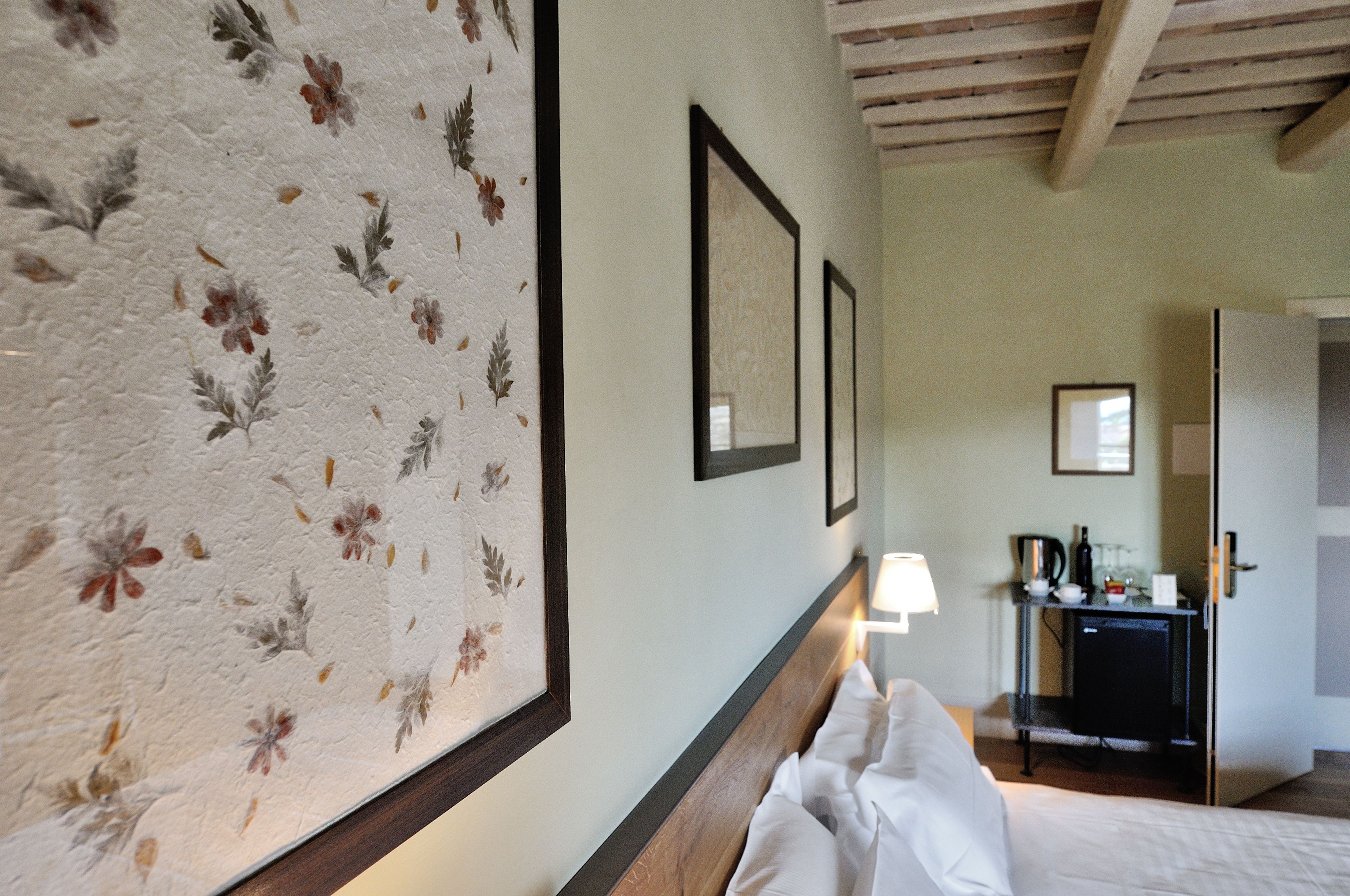 A hotel room with a bed, a nightstand, a desk with a lamp, and framed pictures on the wall.