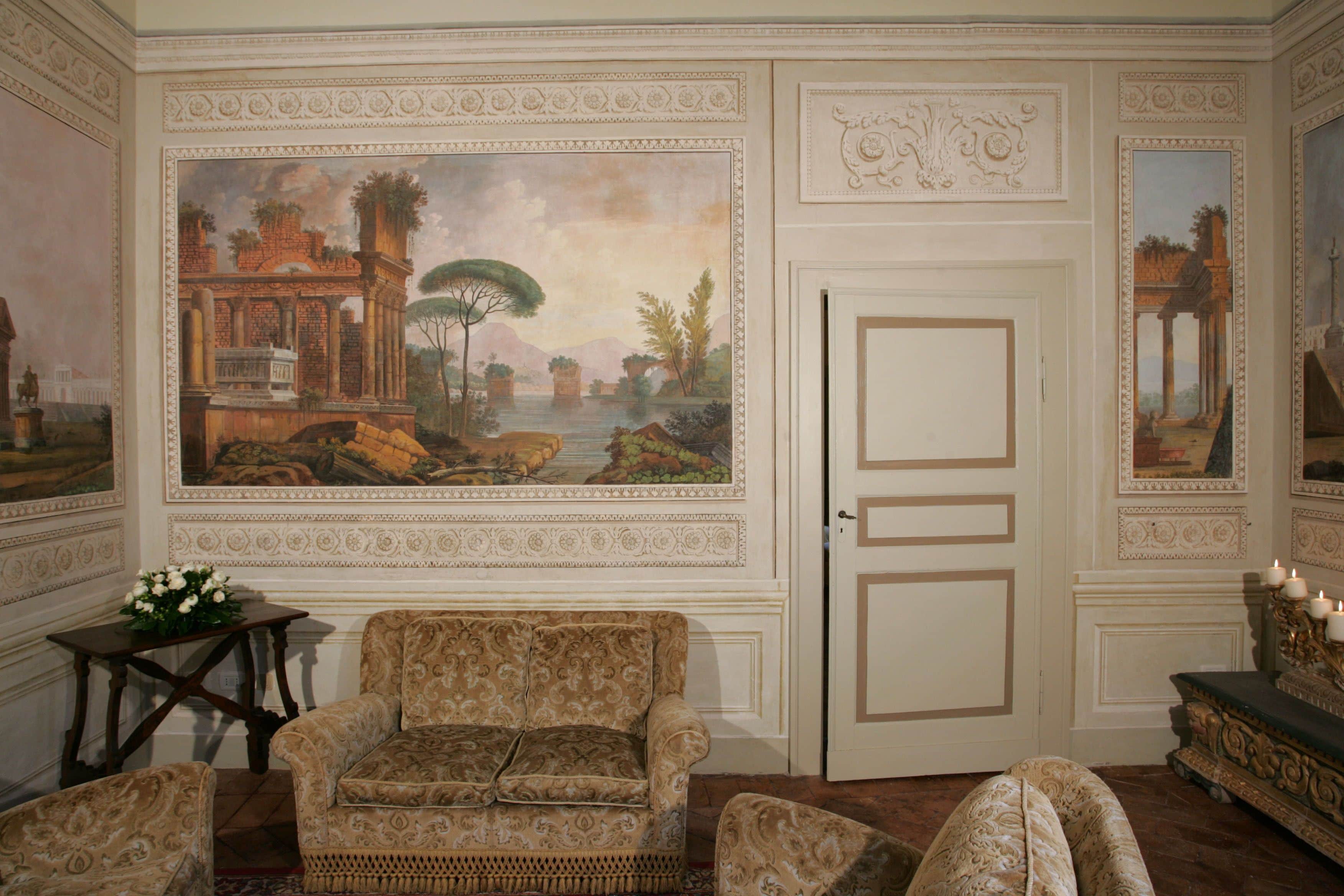 A room with a large mural, a sofa, and a table with flowers.