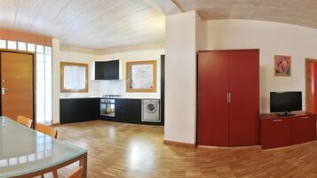 Cocina compacta con lavadora, zona de comedor con mesa de vidrio y un armario rojo.