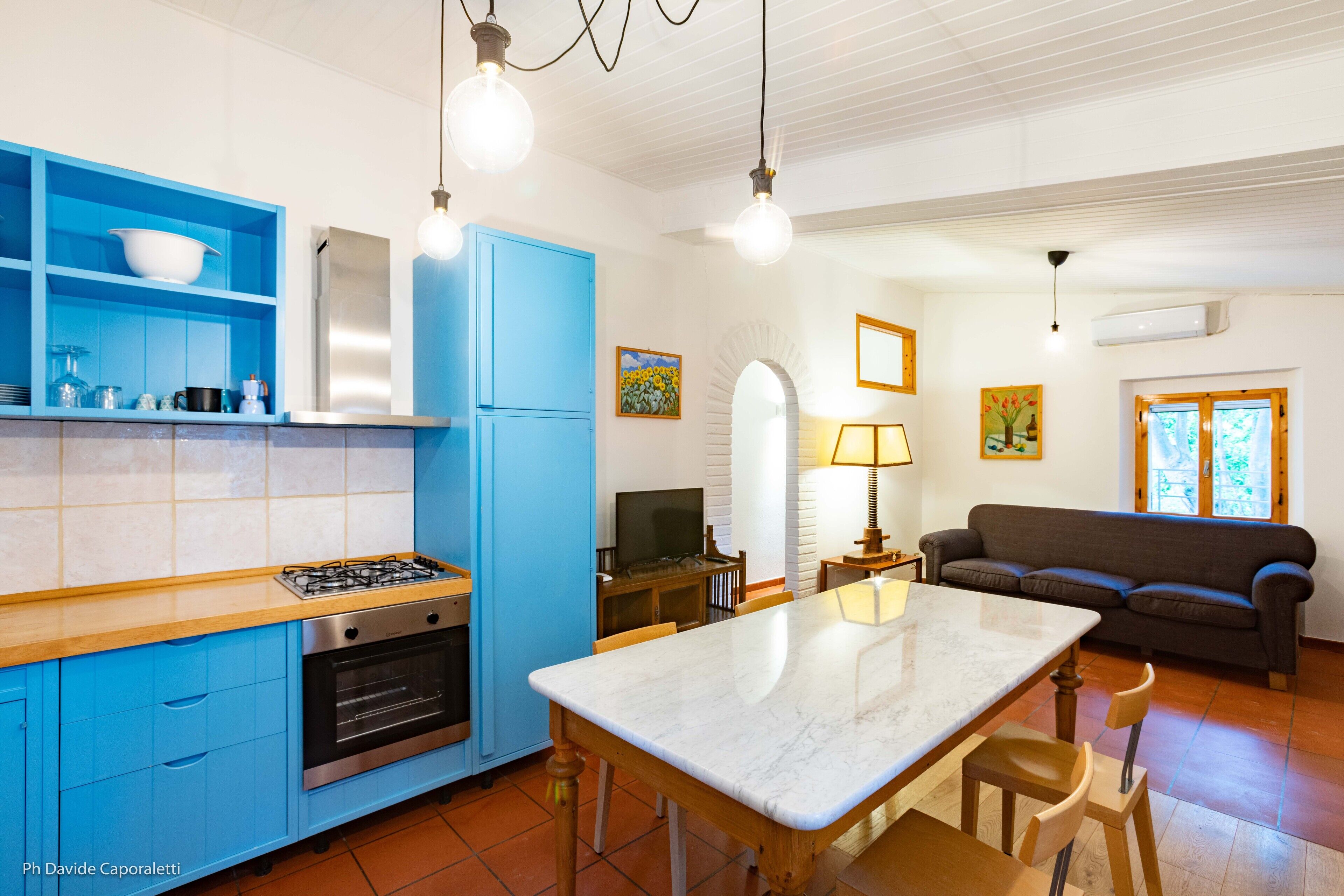 Una cocina moderna con armarios azules, una isla de mármol y una zona de comedor con sofá y lámpara.