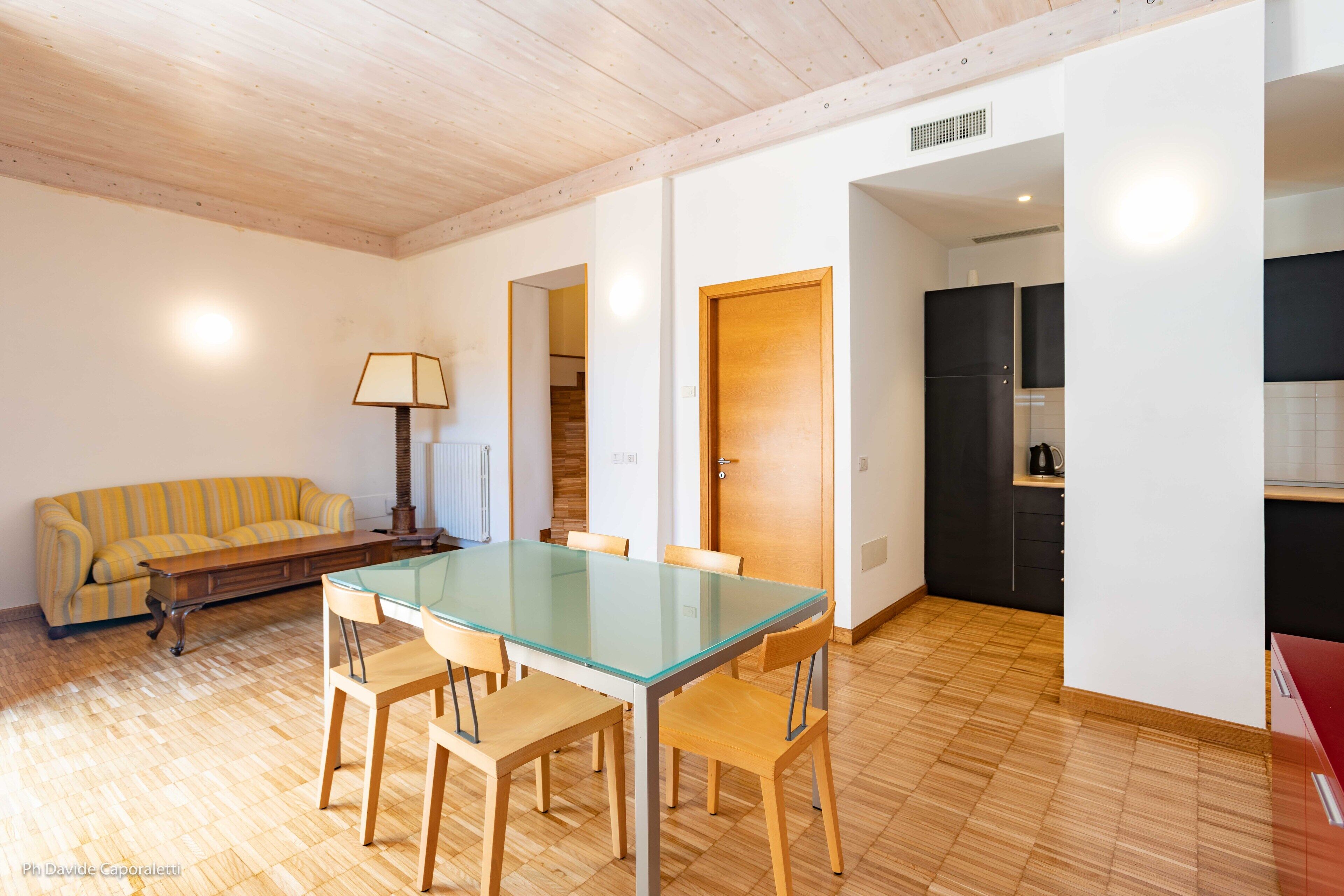 A dining area with a glass-top table and wooden chairs, a yellow striped sofa, and a lamp.