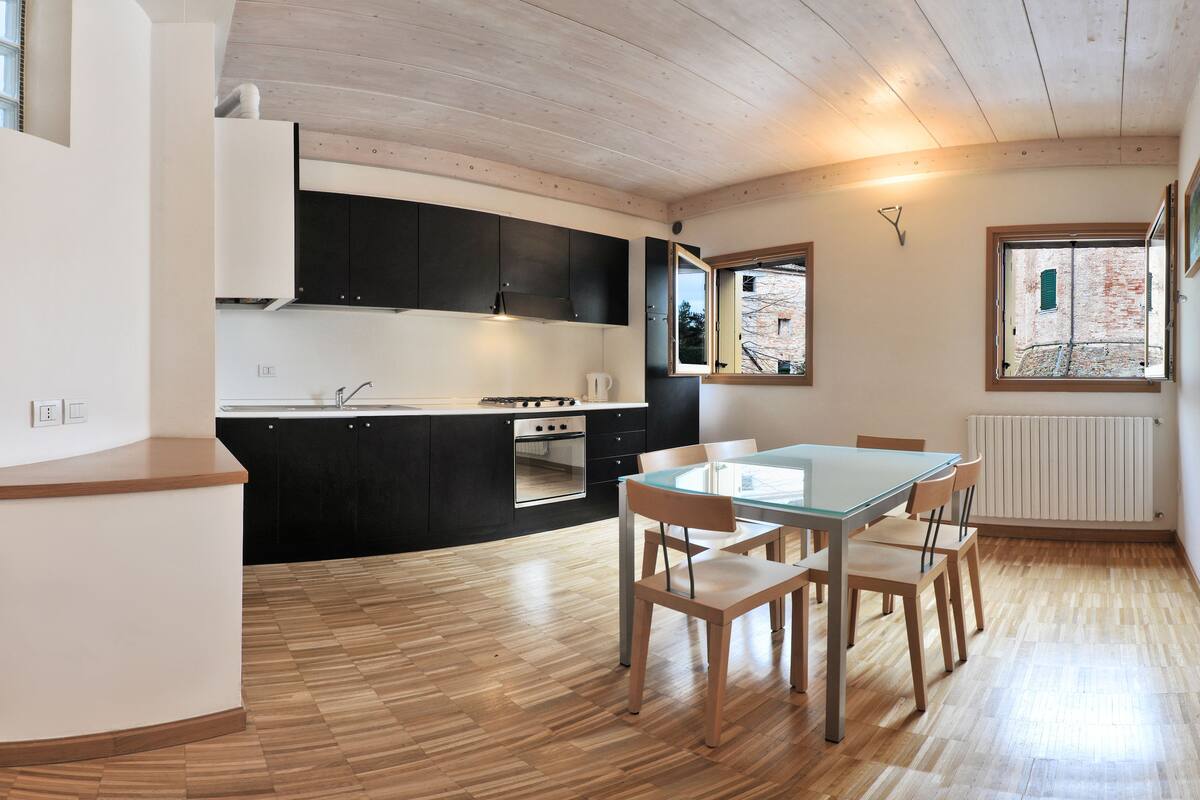 A modern kitchen with black cabinets, a wooden countertop, and a dining area with a glass table and wooden chairs.