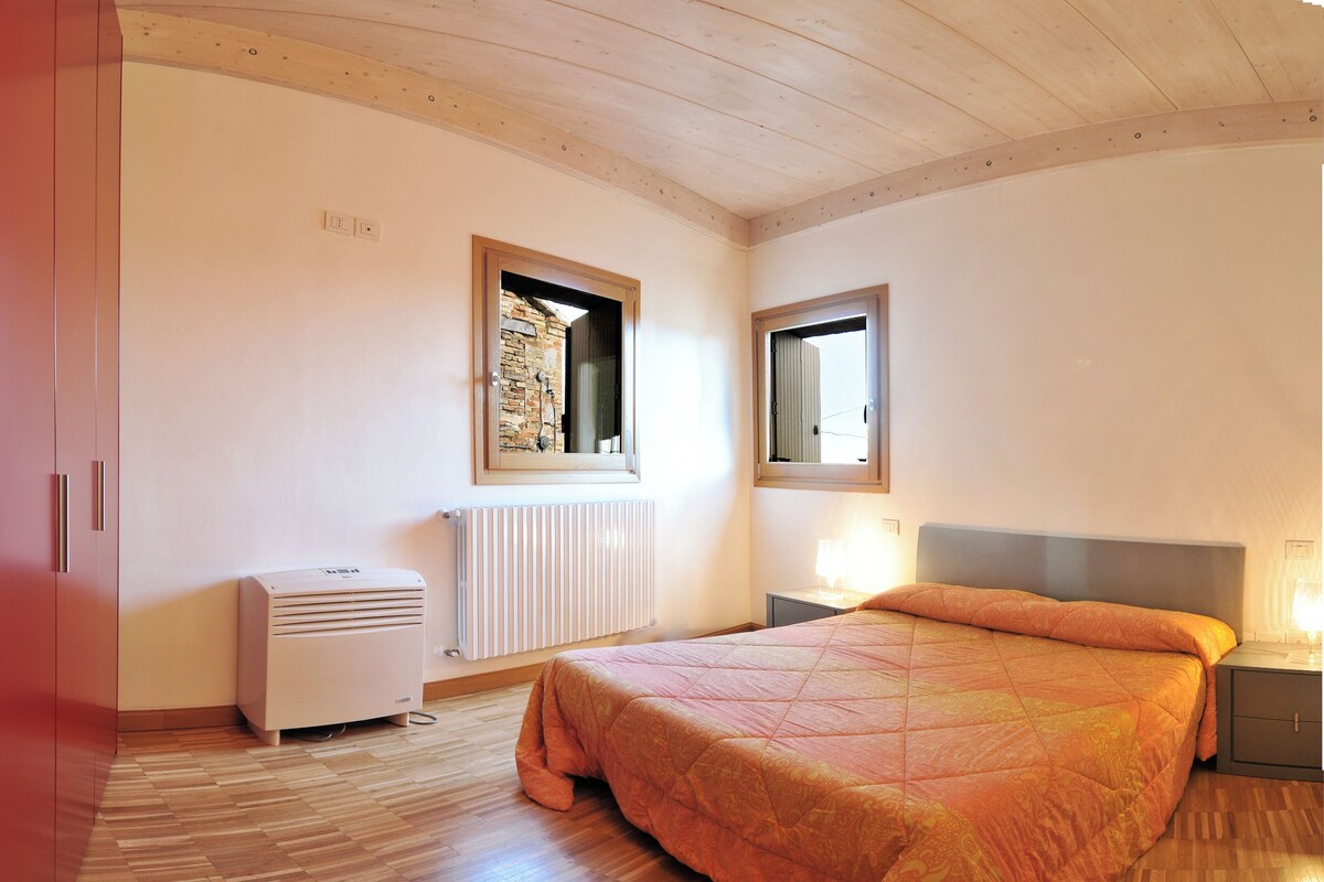 A bedroom with a bed, a radiator, a window, and a wooden ceiling.