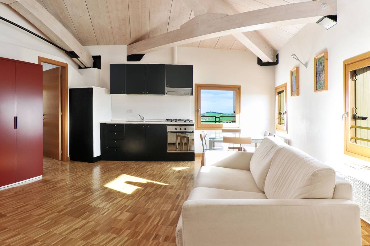 A modern living room with a red cabinet, a white sofa, and a kitchen area with black cabinets and a window.