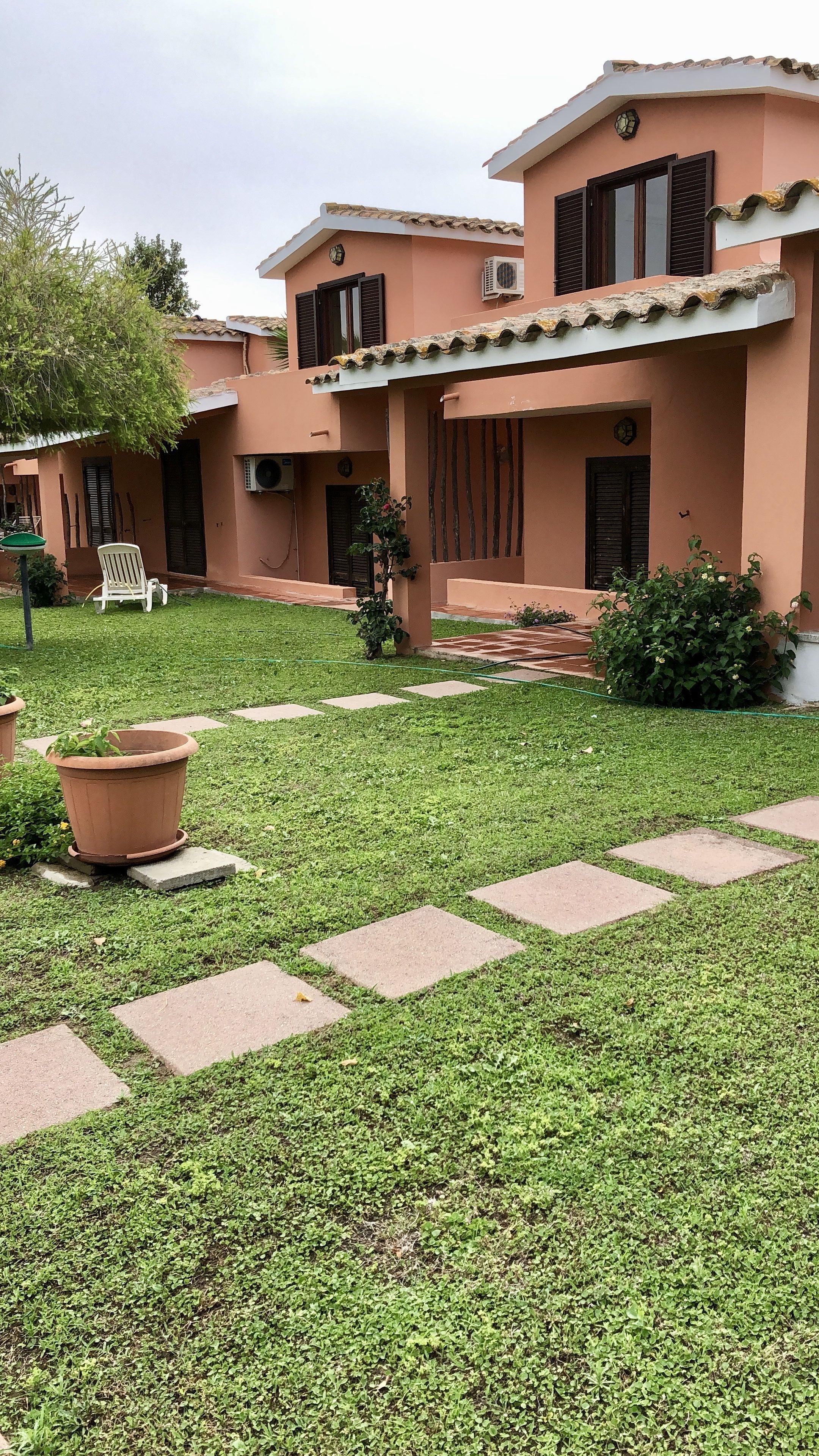 Ein gepflegter Garten mit einem gepflasterten Weg, der zu einem Gebäude mit einem Ziegeldach und verstellbaren Fensterläden führt.