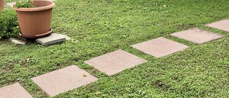 Een verzorgde tuin met een geplaveid pad dat leidt naar een gebouw met een pannendak en luiken.