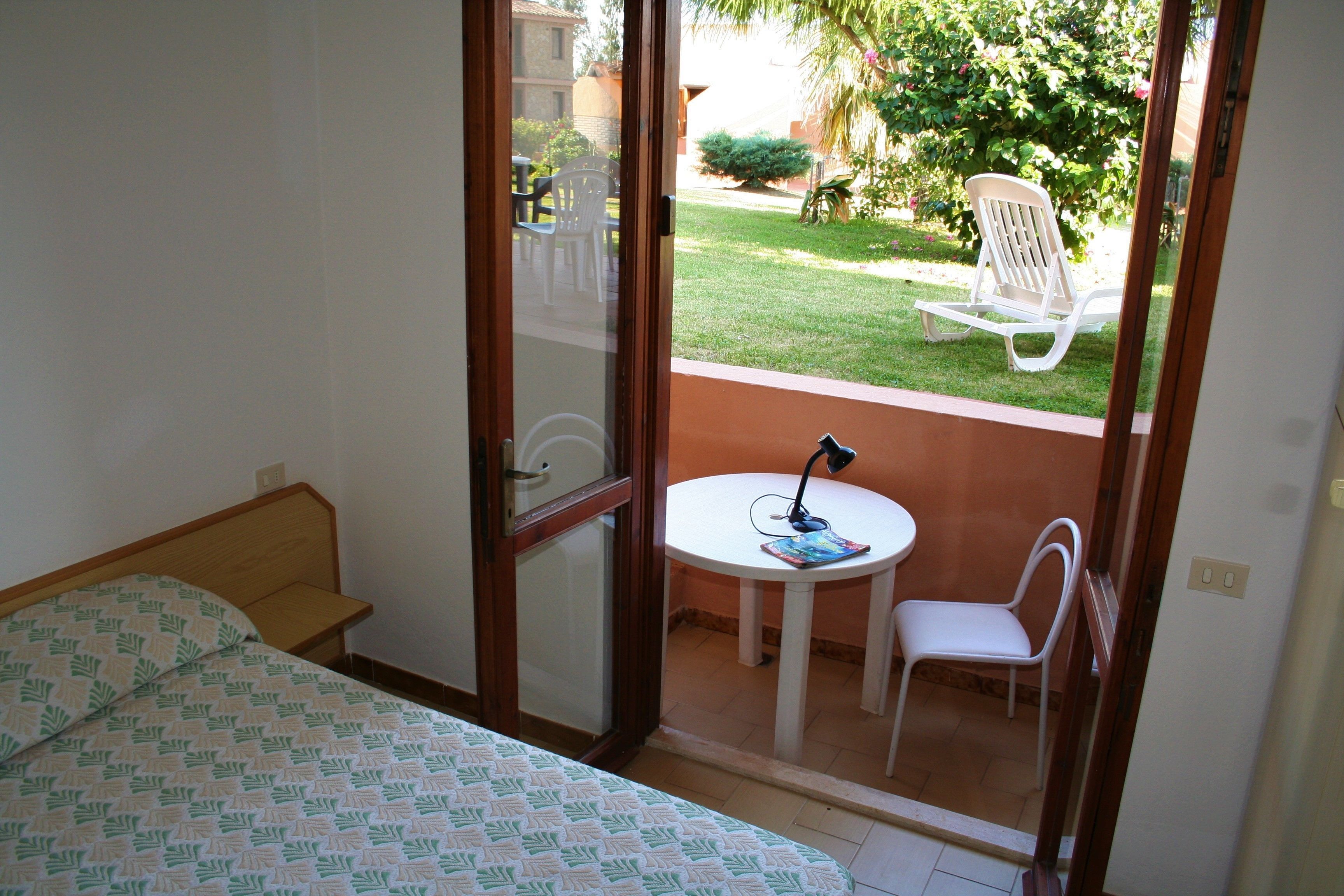 Un dormitori amb un llit, una taula petita amb una cadira i vista a un jardí a través d'una porta de vidre.