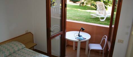 Un dormitori amb un llit, una taula petita amb una cadira i vista a un jardí a través d'una porta de vidre.