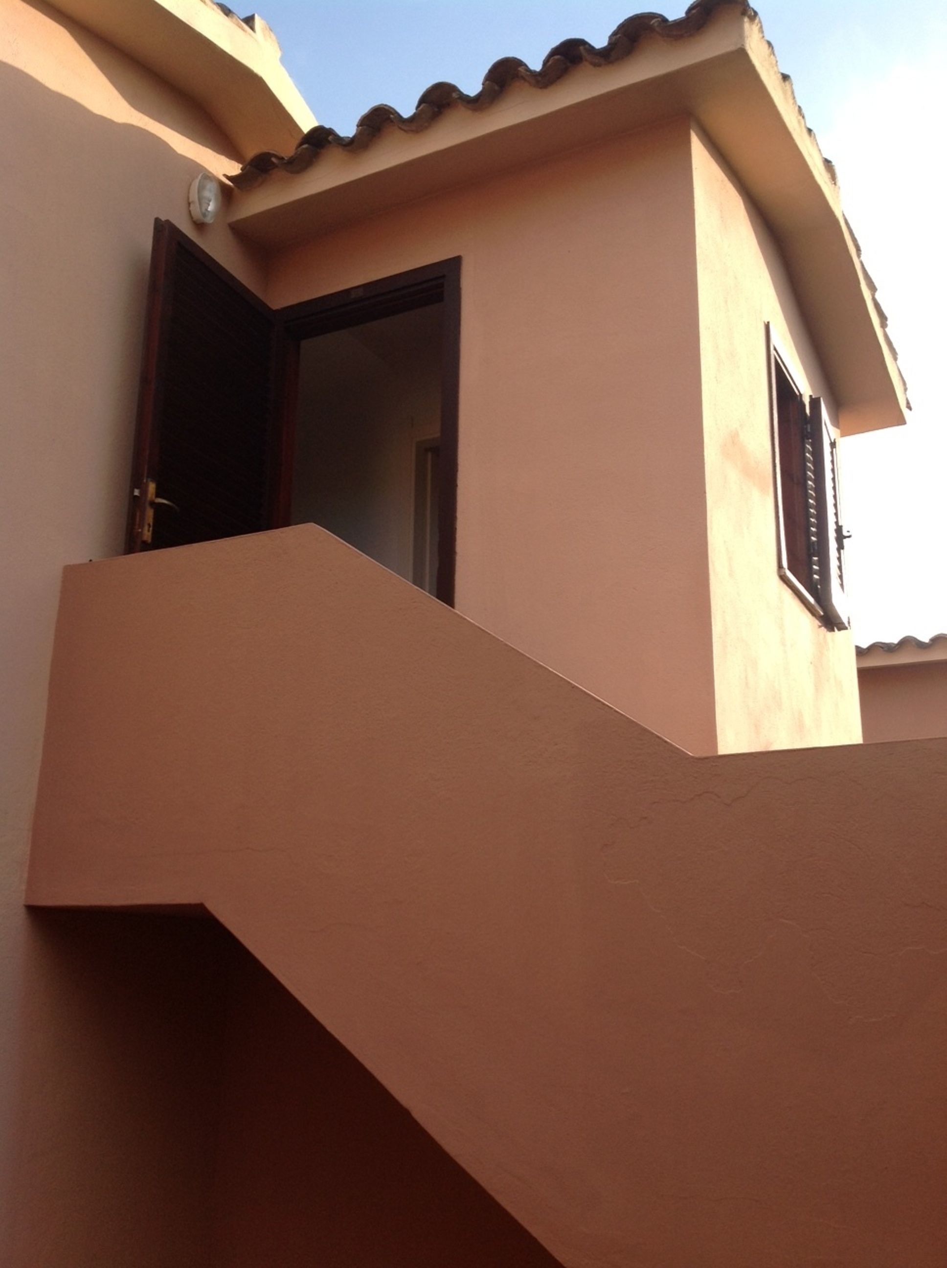 Un edificio con fachada color beige, una puerta y una ventana con contraventanas.