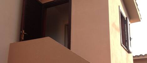 Un edificio con fachada color beige, una puerta y una ventana con contraventanas.