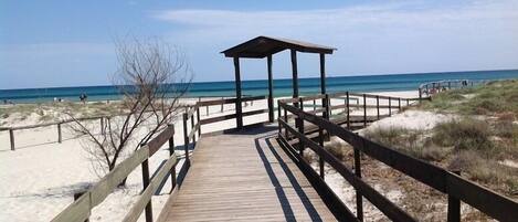 A wooden boardwalk leading to a beach with a covered pavilion.