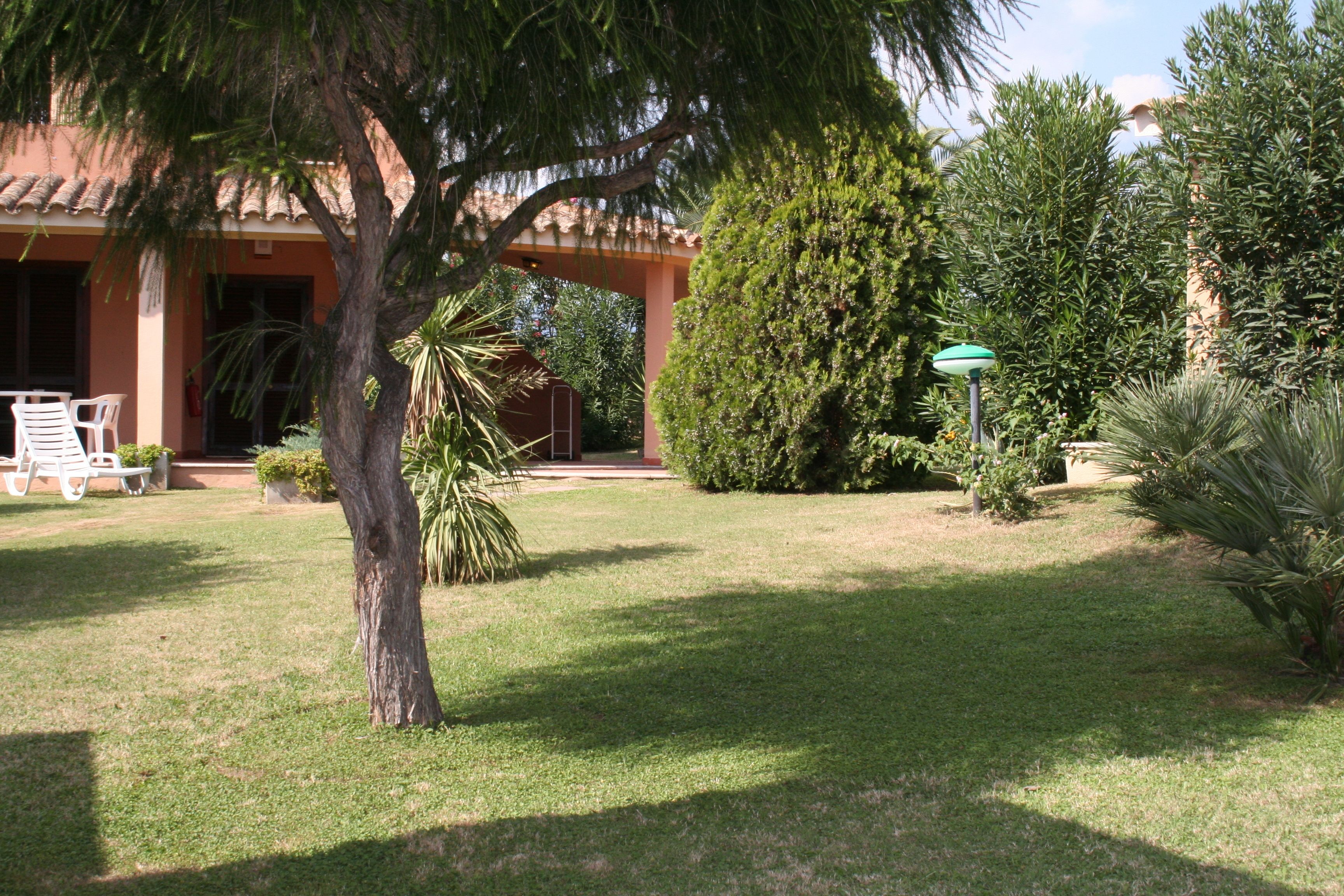 A well-maintained garden with a patio area, a large tree, and a building with a tiled roof.