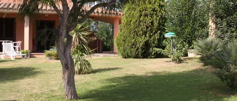 A well-maintained garden with a patio area, a large tree, and a building with a tiled roof.