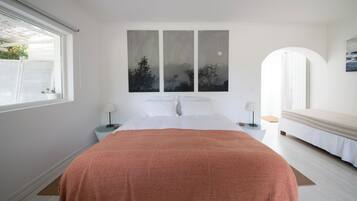 A bedroom with a bed, a nightstand, a lamp, a window, and a painting on the wall.