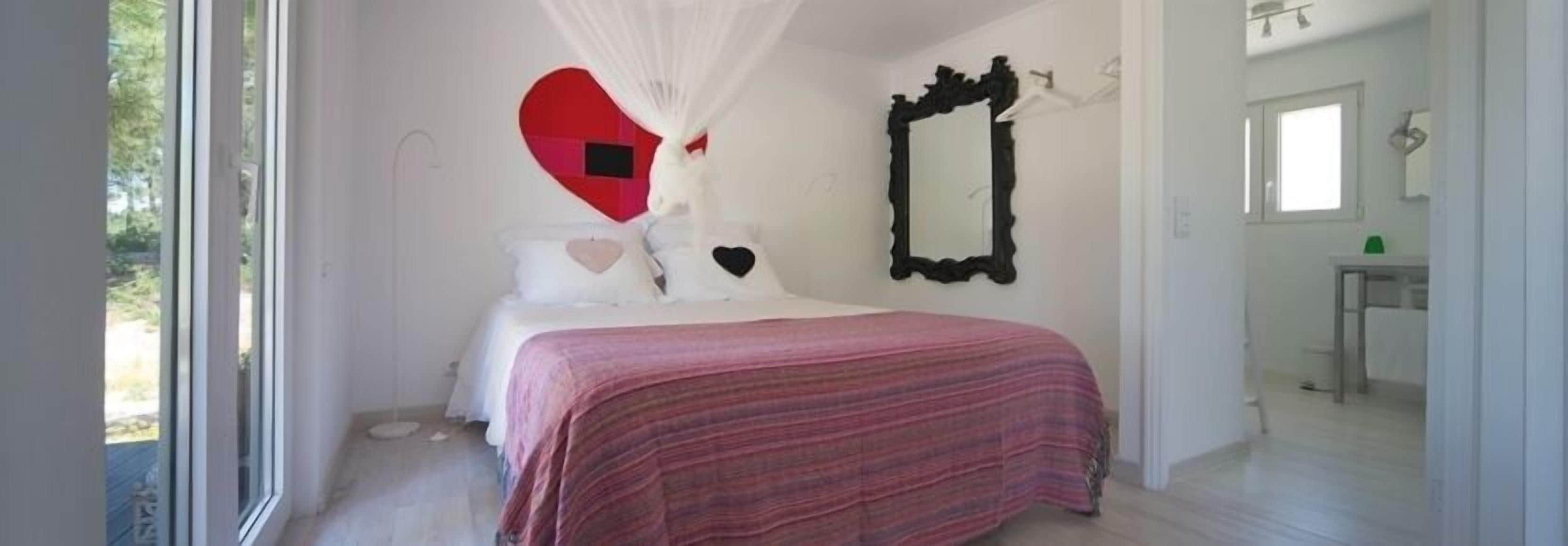 A bedroom with a bed, a mirror, and a heart-shaped decoration on the wall.