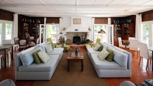 A spacious living room with two sofas, a coffee table, and a fireplace. There are bookshelves and a dining area visible. - Casal do Frade (Sesimbra)