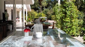 An outdoor dining area with a glass table, a white basket, and a vase with red flowers. - Casal do Frade (Sesimbra)