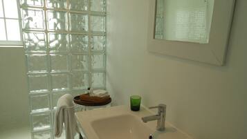 Un baño con cabina de ducha de vidrio, lavamanos con espejo y toallero.