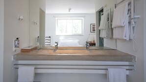 A modern bathroom with a large mirror, a bathtub, and a window providing natural light. - Casal do Frade (Sesimbra)