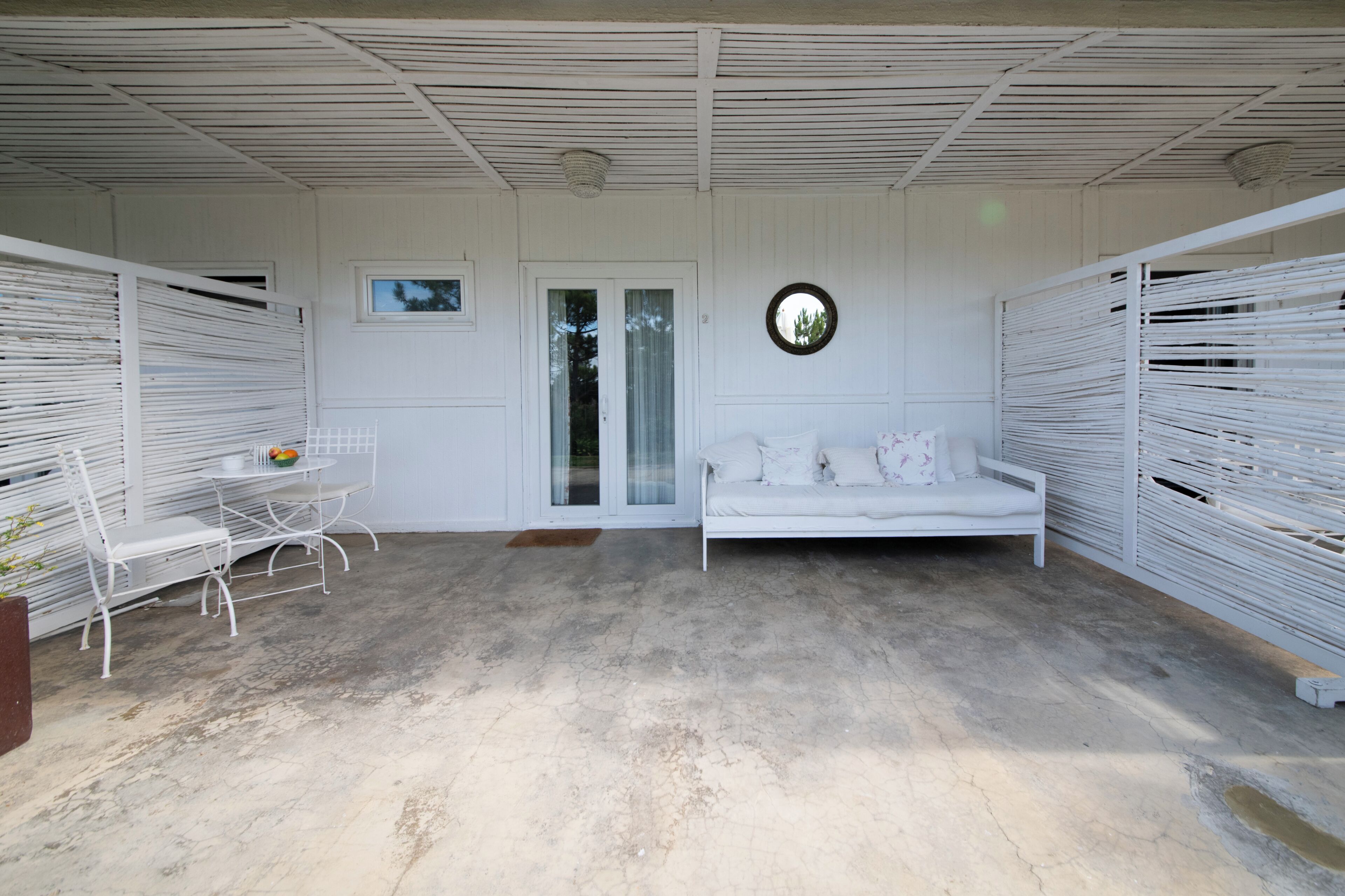 Una habitación blanca con un sofá blanco, una mesita con sillas y una ventana.