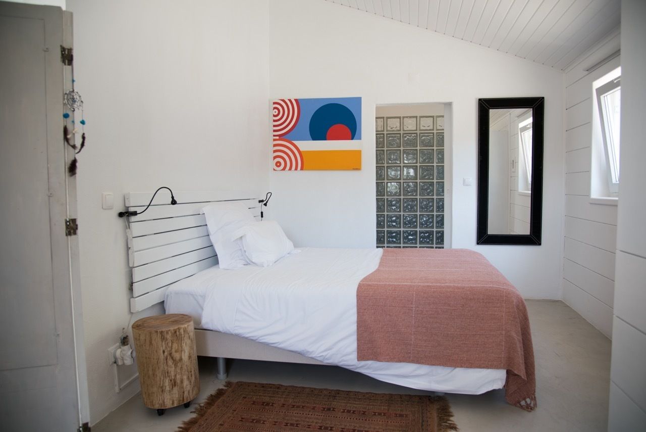 Un dormitorio con cama, una obra de arte en la pared, una ventana con vistas y un espejo.
