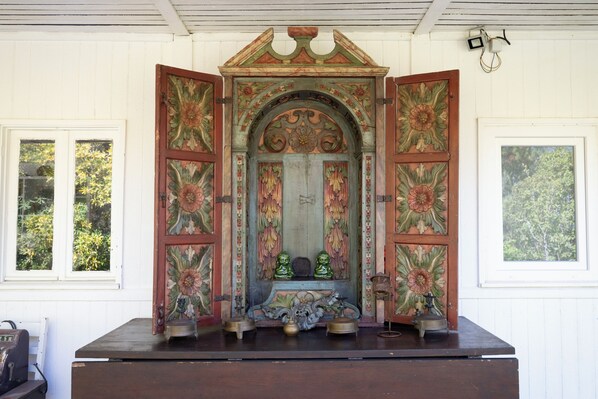 A shrine with a central archway, two doors, and a wooden platform with statues and a bell.