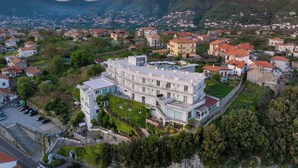 A modern building with a pool, surrounded by lush greenery and a mountainous backdrop. - Hotel Le Rocce (Agerola)