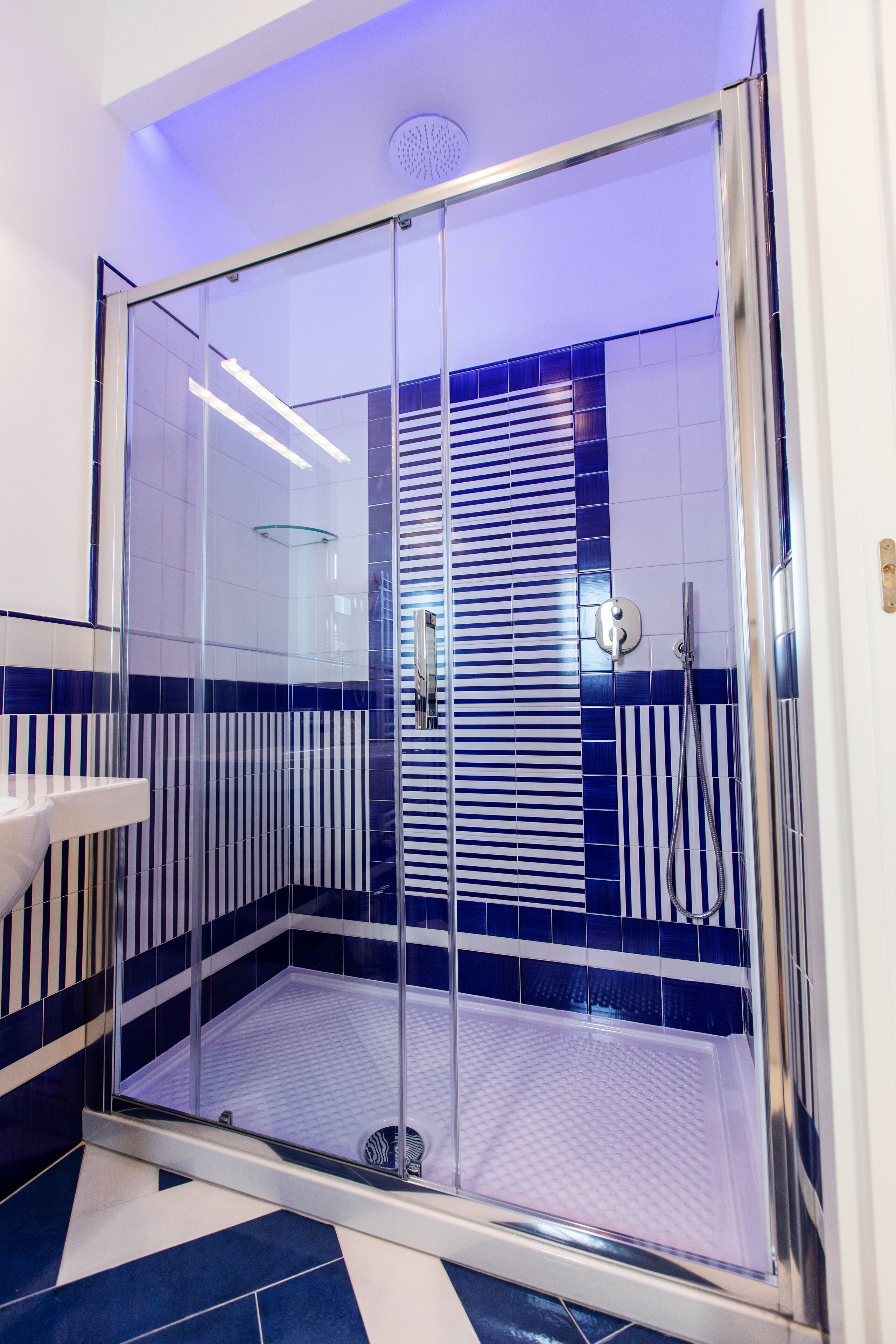 A modern bathroom with a glass-enclosed shower, tiled walls, and a white sink.