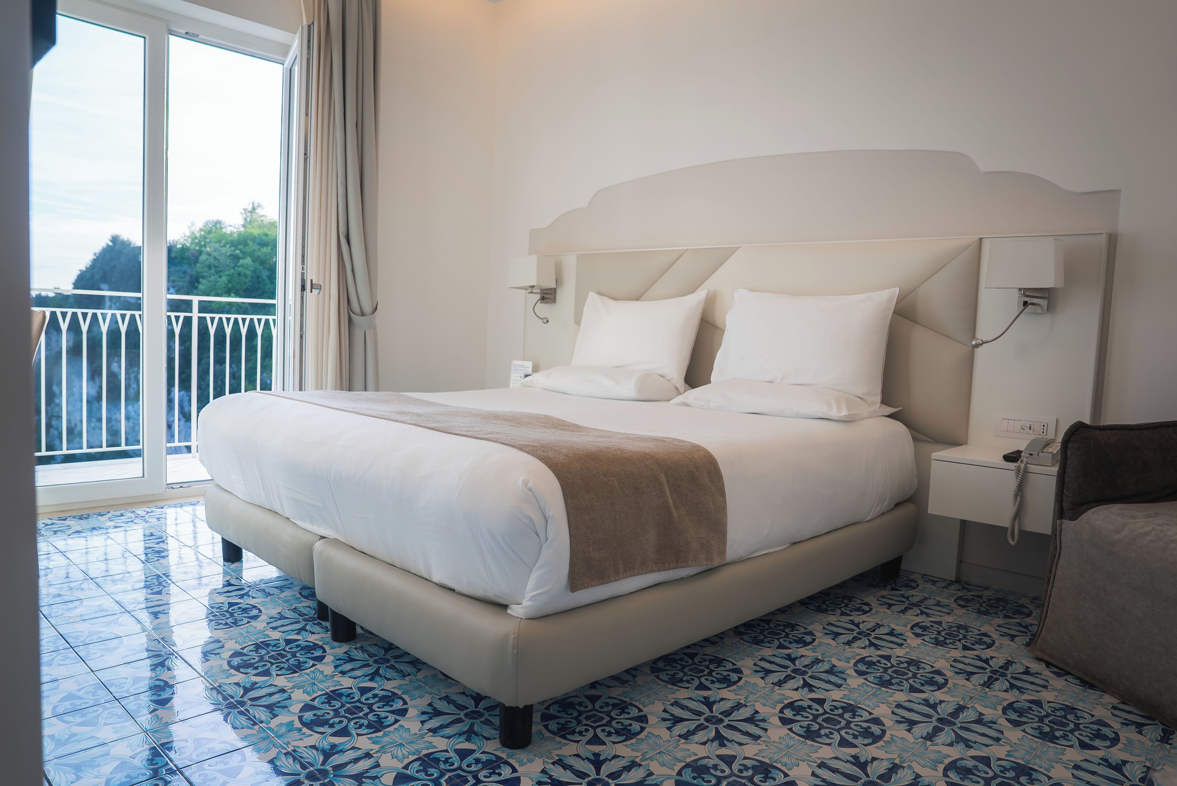 A hotel room with a large bed, a bedside table, a phone, and a view of the outdoors.