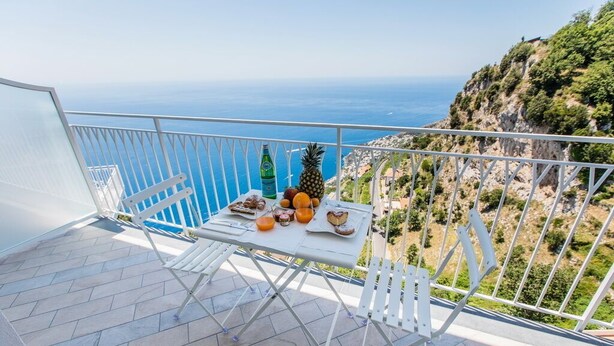 A balcony with a table set for breakfast, overlooking a coastal view. - Hotel Le Rocce (Agerola)