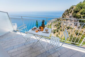 A balcony with a table set for breakfast, overlooking a coastal view.