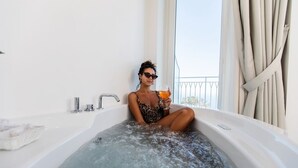 A person in a bathtub filled with water, holding a drink, with a window and curtains in the background. - Hotel Le Rocce (Agerola)